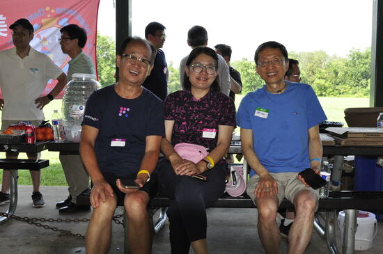 Three attendees seated together on a picnic bench.