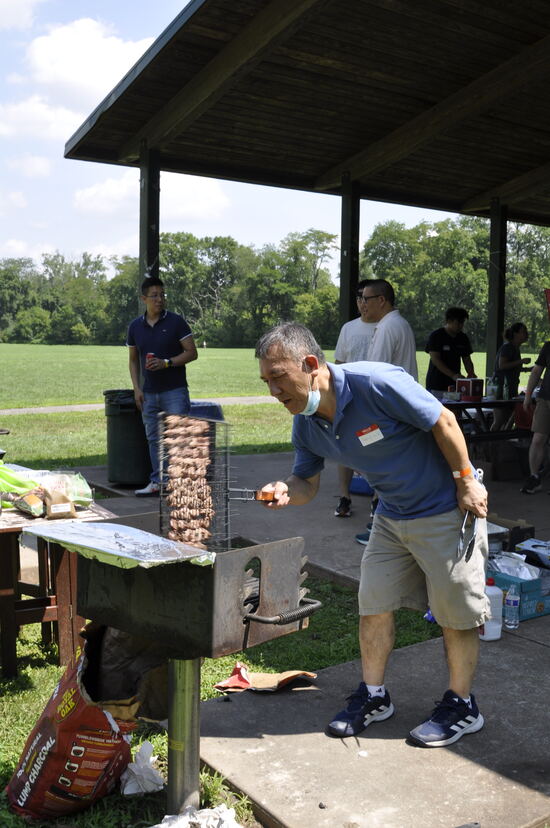 A volunteer tending rows of skewers on a vertical grill.
