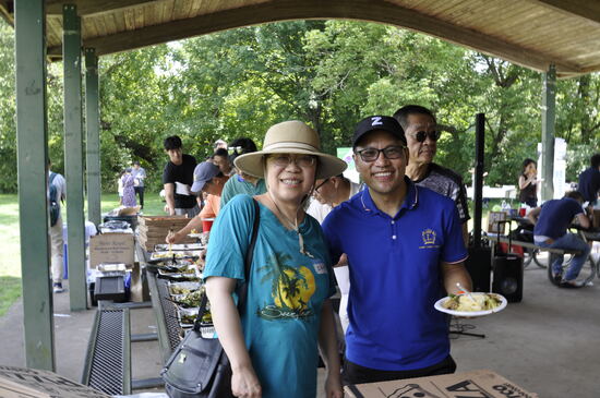 Two attendees with plates of food under the pavilion.