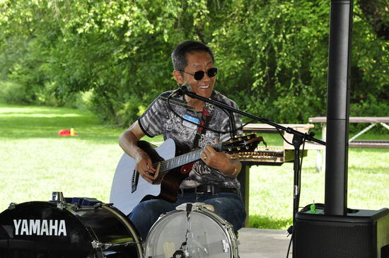 A performer playing acoustic guitar beside the drum kit.